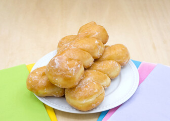 Wall Mural - White porcelain plate with glazed twist donuts on a light wood table with colorful napkins on each side.