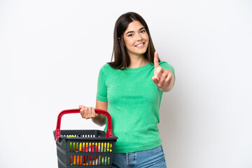 Young Brazilian woman holding a shopping basket full of food isolated on white background showing and lifting a finger