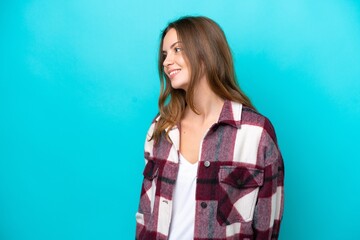 Wall Mural - Young caucasian woman isolated on blue background looking to the side and smiling