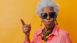 A spirited elderly woman with sunglasses pointing with panache against an orange backdrop.