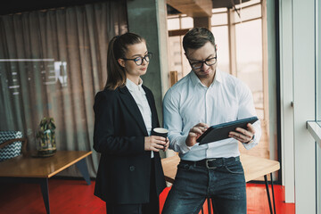 Wall Mural - Happy man wearing eyeglasses and colleague smiling during corporate collaboration, successful employees talking with digital touch pad