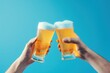 Close up of two hands clinking glasses of beer on blue background.