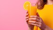 glass of orange juice in female hands on a pink background.