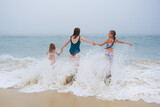 Fototapeta Kwiaty - Mother and children playing on the ocean beach. Family enjoying the ocean. Mother holds girls's hands and they all look at the ocean together.