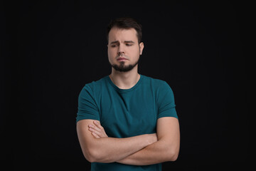 Wall Mural - Portrait of sad man with crossed arms on black background