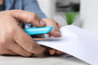 © New Africa - Man with papers using stapler at white table indoors, closeup