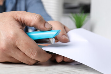 Wall Mural - Man with papers using stapler at white table indoors, closeup