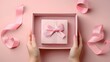 Elegantly poised, hands present a sophisticated pink gift box adorned with a shimmering ribbon, set against a harmonious pink background embellished with decorative elements.