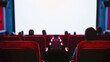 Blank white screen, red chairs, and blurred silhouettes in cinema