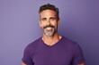 Portrait of handsome mature man smiling and looking at camera while standing against purple background
