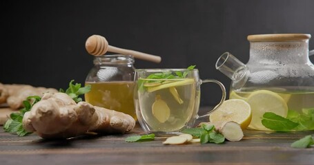 Wall Mural - woman puts mint leaves into glass mug with lemon and ginger hot steaming organic herbal tea