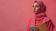 Full length portrait Charming young woman with hijab thinking while holding book on Coral background professional photography.
