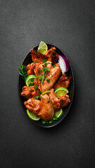 Wall Mural - Fried chicken wings with lime, rosemary and onions. In a black plate. On a dark background.