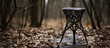 A wooden stool is placed in the center of a forest surrounded by fallen leaves and grass. The natural tints and shades of the environment blend with the hardwood flooring underneath