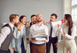 © Studio Romantic - Portrait of peaceful smiling confident young man company employee holding a pile of documents standing in office with a group of noisy screaming in megaphone colleagues. Deadline and overwork concept