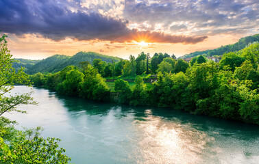 beautiful landscape of spring or summer sunset river with blue water and green hills on sides and mountains with amazing cloude sky on background