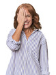 Redhead mid-aged Caucasian woman in studio having fun covering half of face with palm.