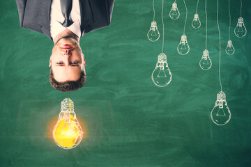 Aufkleber - Upside down portrait of thoughtful man with drawn light bulbs on chalkboard wall background. Idea, inspiration and think outside the box concept.