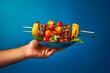 A hand holding a skewer of grilled tropical fruits over a barbecue against a solid blue backdrop, showcasing the vibrant colors and flavors of the Tropical vacation-themed food and bevera