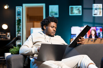 Poster - Remote employee concentrating on finishing up important job tasks, reading files info in apartment personal office. Focused teleworker crosschecking documents between laptop and paperwork