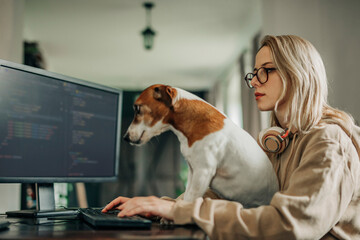 Software programmer coding on computer near dog at home office
