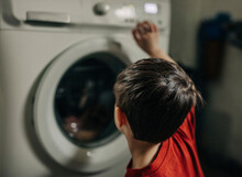 Boy Operating Washing Machine In Utility Room At Home