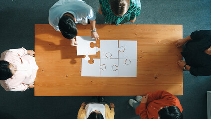 Wall Mural - Top down view of skilled business people assemble jigsaw puzzle on meeting table. Group of diverse team working together to solve the puzzle. Represented unity, togetherness, cooperative. Convocation.