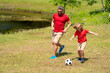 © Volodymyr - Father and son playing football in park. Dad and little boy play soccer. Sporty family enjoy summer day. Sport for kids. Football soccer game. Fathers day. Father and son kick ball on the green grass.
