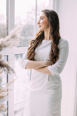 curly-haired woman in a white dress looks out the window