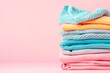 Pile of knitted sweaters and cozy scarves on pink background with copy space, Stack of clothes