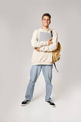 Wall Mural - smiling handsome man in his 20s with laptop confident standing against grey background
