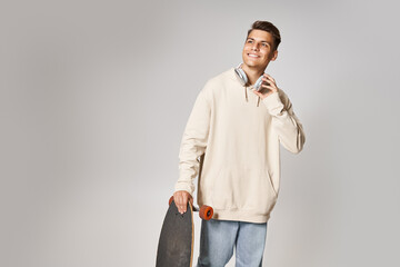 Wall Mural - smiling young man in headphones with skateboard looking to up on light background