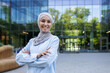 A professional woman in a hijab stands confidently with crossed arms outside a contemporary office building, symbolizing empowerment and diversity in the workplace.