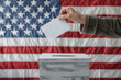 Ballot held by a hand, backdrop of an American flag, democratic process and elections in the USA