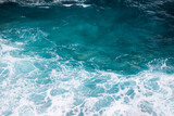 Fototapeta  - Turquoise waters churn white foam around dark rocky outcrops on a bright sunny day