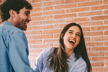 Happy young adult couple at home celebrating happy hugging against a brick wall background. People man and woman have fun together with celebration and joyfuil expression