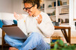 © simona - One excited happy woman doing video call using laptop at home sitting barefoot on the floor. Female gesturing with hands in front of a computer and videocall conference. Online meeting dating website