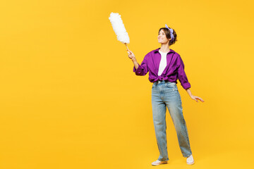 Full body young smiling happy woman she wear purple shirt do housework tidy up hold duster wipe sweep away dust look camera isolated on plain yellow background studio portrait. Housekeeping concept