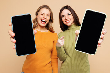 Wall Mural - Young friend two women they wear orange green shirt casual clothes together hold use close up mobile cell phone with blank screen workspace area isolated on plain beige background. Lifestyle concept.