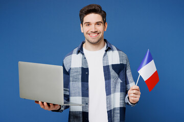 Wall Mural - Young smiling happy IT man wears shirt white t-shirt casual clothes hold in hand French flag use work on laptop pc computer isolated on plain blue cyan background studio portrait. Lifestyle concept.