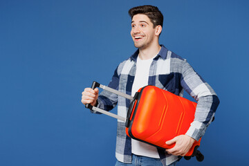 Poster - Side view traveler man wear shirt casual clothes hold suitcase bag look aside isolated on plain blue background. Tourist travel abroad in free spare time rest getaway. Air flight trip journey concept.