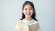 A happy Asian girl is reading a beige book and laughing on a plain white background with copy-space for text.