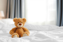 Cute Little Teddy Bear Lying Alone On White Bed In Morning