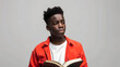 A sad black teenage boy is reading a brown book on a plain gray background with copy-space for text.