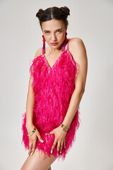 Wall Mural - Radiant brunette woman in pink feather outfit holding her dress and looking to camera confidently