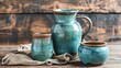 Rustic still life with handmade ceramic jug, cup and bowl. The pottery is glazed in a blue-green color and has a rough, textured surface.