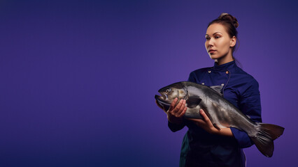 An assertive chef in a dark blue uniform confidently presents a large fish, showcasing a specialized seafood culinary skill