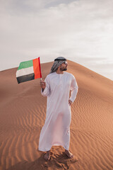 Wall Mural - Arab man holding UAE flag walking in the desert ,national day celebration - spirit of the union 