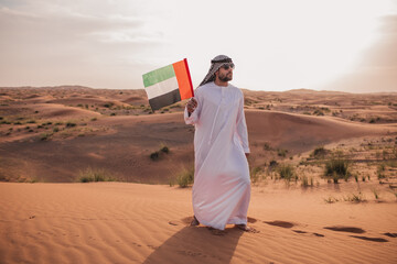 Arab man holding UAE flag walking in the desert ,national day celebration - spirit of the union 