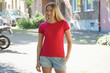 Young blonde woman wears a red t-shirt with copy space or text space for print or design outdoors in a city	
